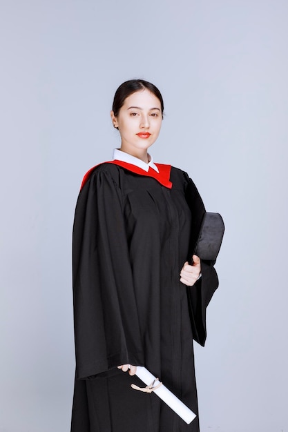 Joven estudiante con bata y diploma posando para el día de graduación. Foto de alta calidad