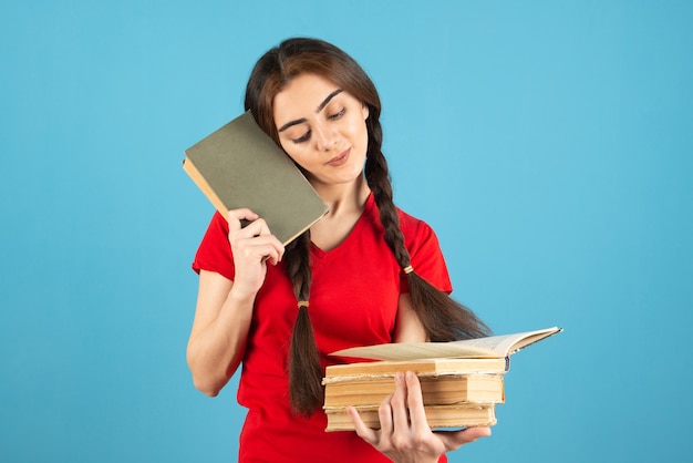 Joven estudiante en camiseta roja leyendo un nombre de libro en la pared azul.