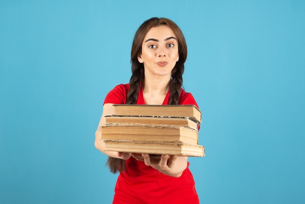 Joven estudiante en camiseta roja ofreciendo libros sobre pared azul.