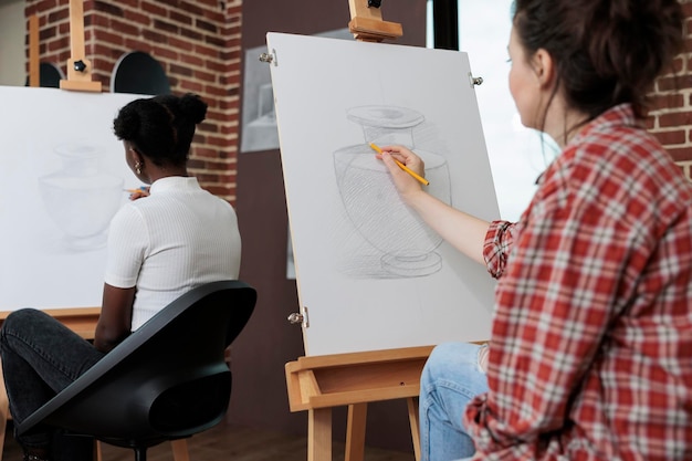 Joven estudiante dibujando jarrón artístico sobre lienzo de pintura trabajando en técnica de ilustración usando lápiz gráfico durante la lección de arte en el estudio de creatividad. Equipo multiétnico que desarrolla la habilidad creativa