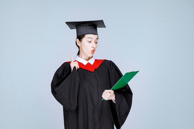 Joven estudiante graduada mirando diploma. Foto de alta calidad
