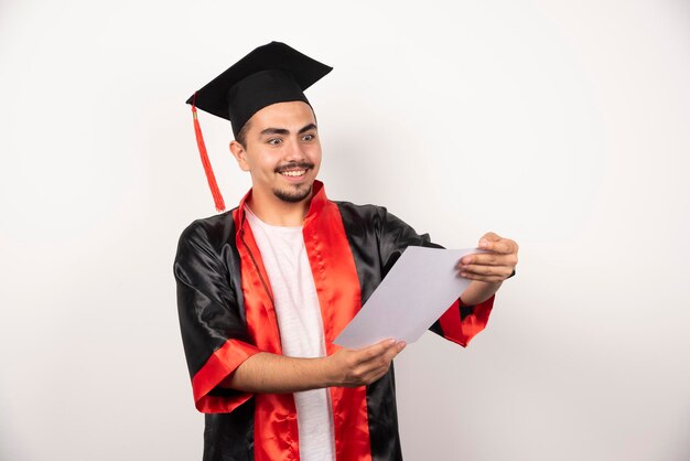 Joven estudiante graduado mirando felizmente diploma en blanco.