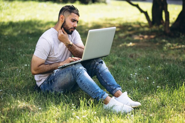 Joven estudiante guapo con computadora portátil en un parque de la Universidad