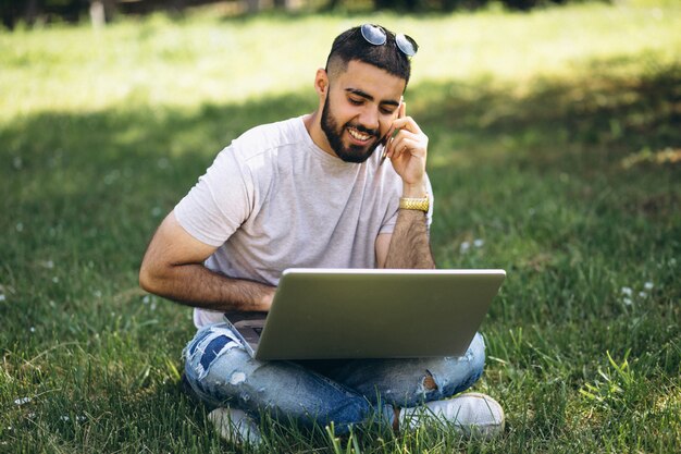 Joven estudiante guapo con computadora portátil en un parque de la Universidad