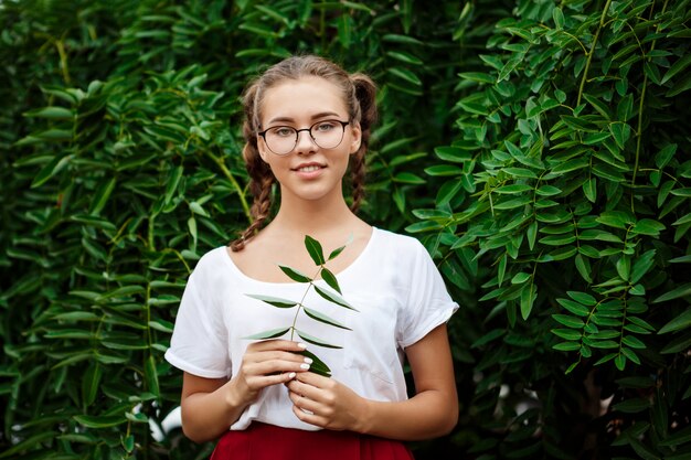 Joven estudiante hermosa en gafas sonriendo, posando sobre las hojas al aire libre.