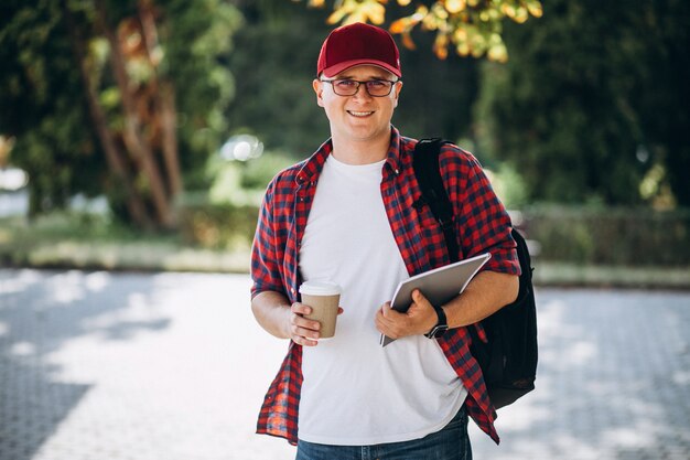 Joven estudiante masculino tomando café con el portátil en el parque