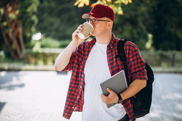 Joven estudiante masculino tomando café con el portátil en el parque