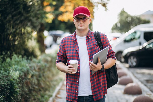 Joven estudiante masculino tomando café con el portátil en el parque