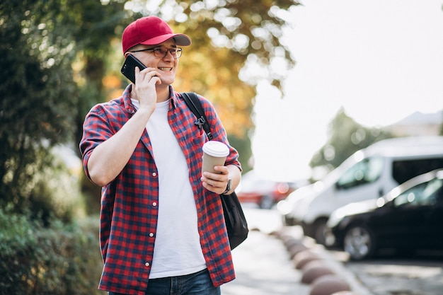 Joven estudiante masculino tomando café usando el teléfono en el parque