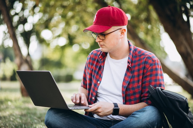 Joven estudiante masculino trabajando en una computadora en el parque