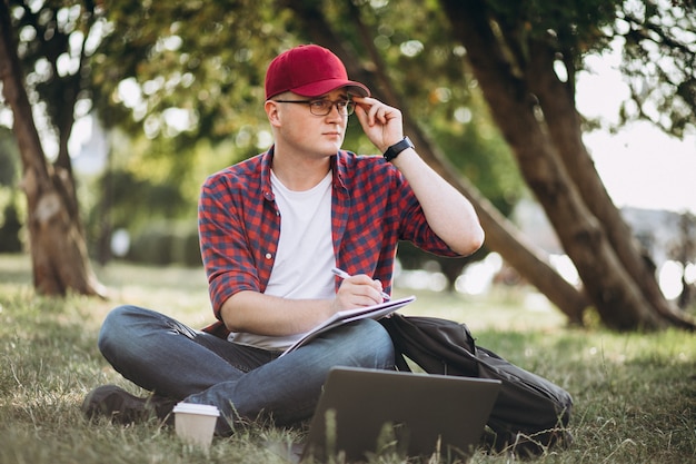 Joven estudiante masculino trabajando en una computadora en el parque