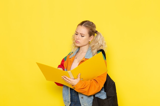 joven estudiante en ropa moderna sosteniendo archivos amarillos sobre amarillo