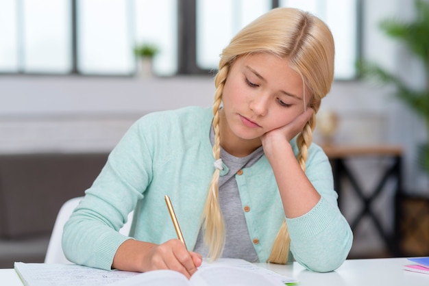 Foto gratuita joven estudiante rubia que parece aburrida y escribiendo