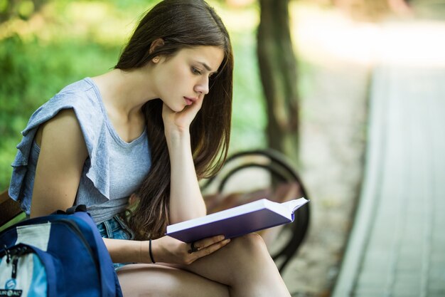 Joven estudiante sentada en un banco y libro de lectura en el parque