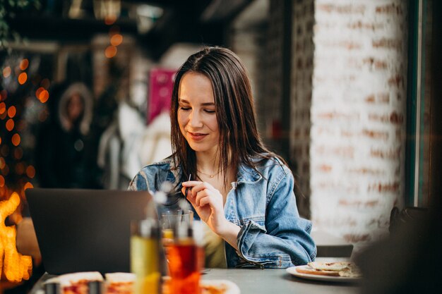 Joven estudiante trabajando en la computadora portátil en el bar y comiendo pizza