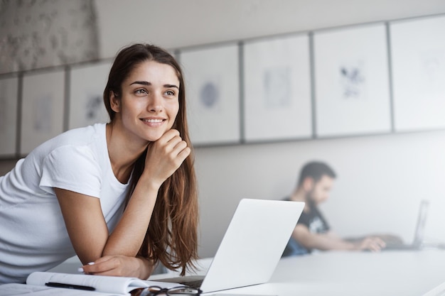 Joven estudiante universitaria que usa una computadora portátil para escribir un diploma