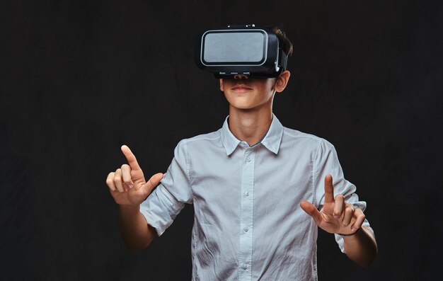 Joven estudiante vestido con una camisa blanca con gafas de realidad virtual. Aislado en el fondo oscuro.