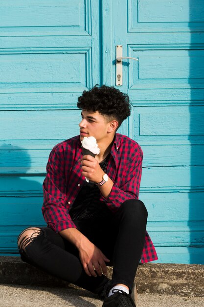 Joven étnico sentado sosteniendo helado en camisa a cuadros