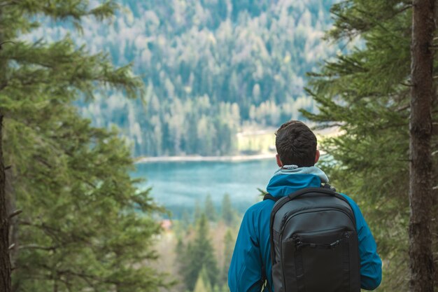 Joven excursionista anónimo con mochila mira un lago de montaña en los Alpes