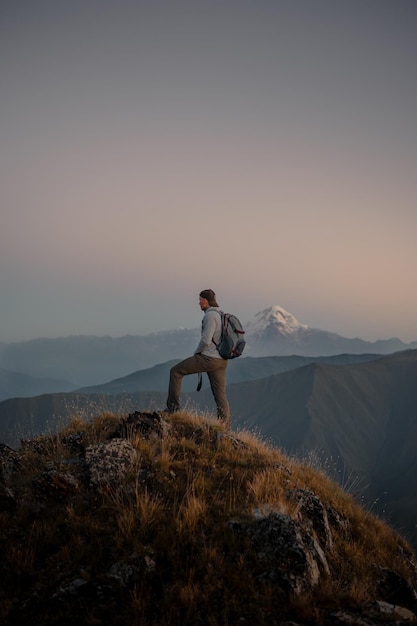 Foto gratuita joven excursionista caucásico de pie en la cima de una montaña cubierta de hierba y admirando la naturaleza brumosa