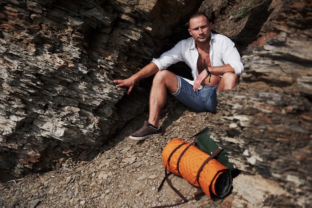 Joven excursionista masculino con mochila relajante en un macizo rocoso durante la tranquila puesta de sol de verano. Concepto de vacaciones de aventura de estilo de vida de viaje