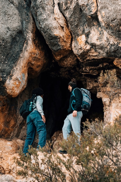 Joven excursionista masculino con su mochila de pie delante de la cueva rocosa