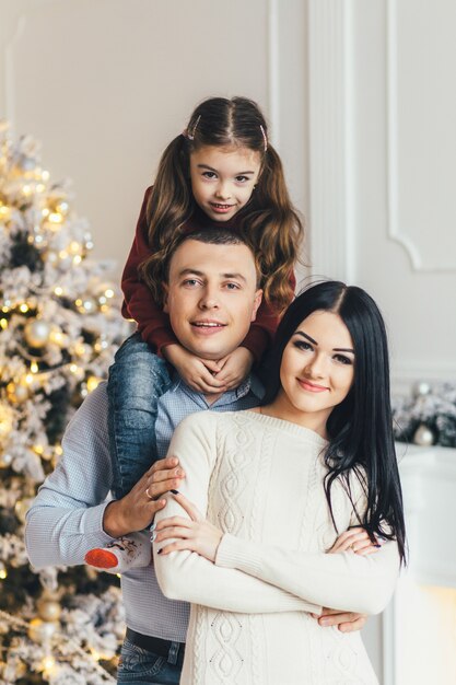 Joven familia posa delante de un brillante árbol de Navidad en una acogedora habitación de lujo