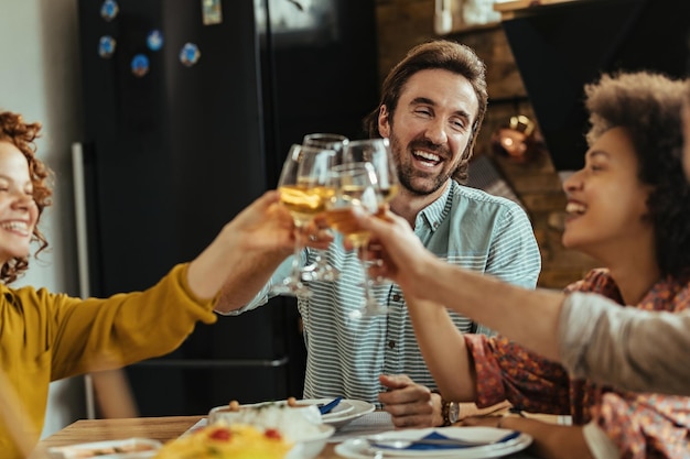 Joven feliz divirtiéndose mientras brinda con sus amigos durante el almuerzo en la mesa del comedor.