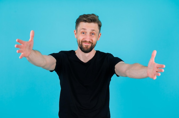 Un joven feliz está abriendo los brazos extendiéndolos a la cámara con fondo azul