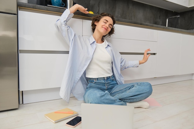 Foto gratuita una joven feliz estira sus brazos, se sienta en el suelo con una computadora portátil y termina su trabajo remoto