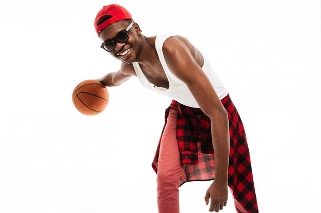 Joven feliz en gafas de sol jugando con pelota de baloncesto