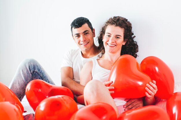 Joven feliz hombre y mujer entre globos en forma de corazones