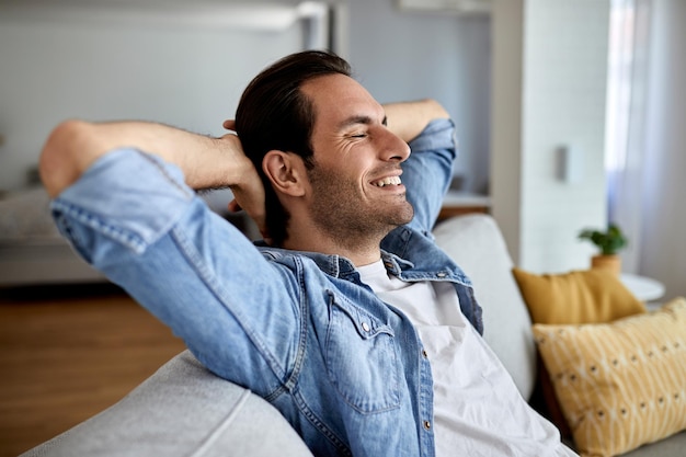 Foto gratuita joven feliz con las manos detrás de la cabeza relajándose en el sofá de casa