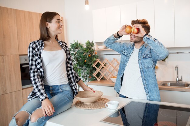 Joven feliz y mujer en la cocina, desayuno, pareja divirtiéndose juntos en la mañana, sonriendo, sosteniendo la manzana, divertido, loco, riendo