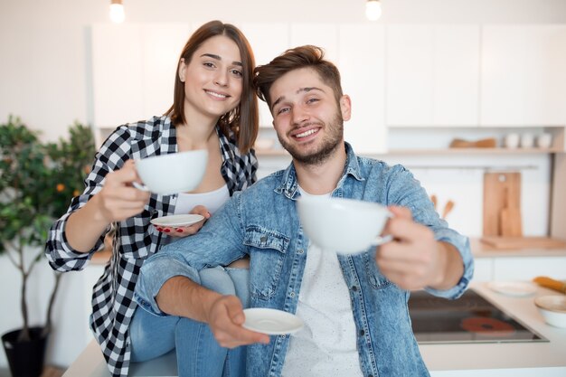 Joven feliz y mujer en la cocina, desayuno, pareja juntos en la mañana, sonriendo, tomando té