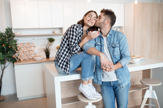 Joven feliz y mujer en la cocina, desayuno, pareja juntos en la mañana, sonriendo, tomando té