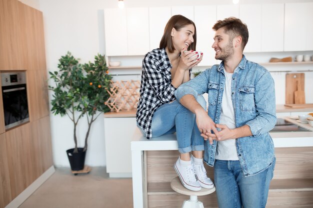 Joven feliz y mujer en la cocina, desayuno, pareja juntos en la mañana, sonriendo, tomando té