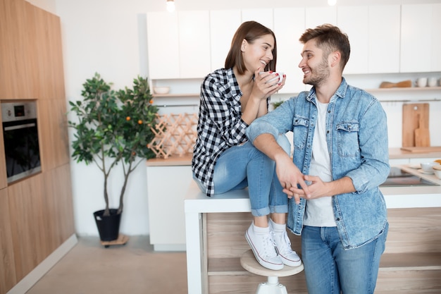 Joven feliz y mujer en la cocina, desayuno, pareja juntos en la mañana, sonriendo, tomando té