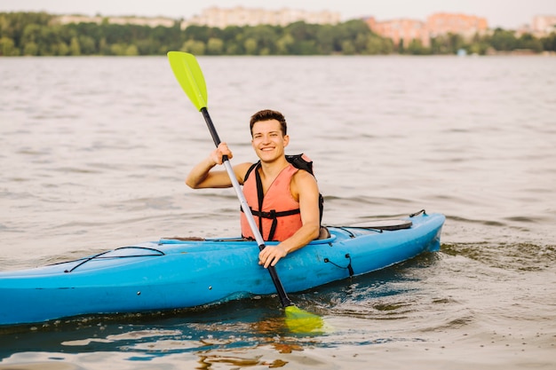 Joven feliz con paddle kayak en el lago