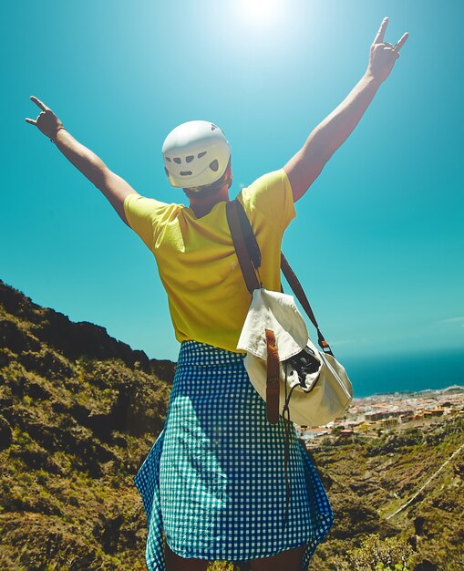 Joven feliz en ropa elegante en la cima de la montaña alcanza el sol