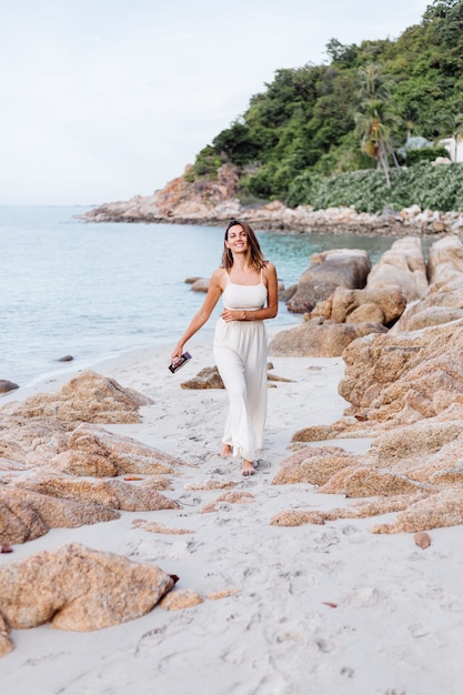 Joven feliz tranquila mujer caucásica con ukelele en la playa rocosa tropical al atardecer