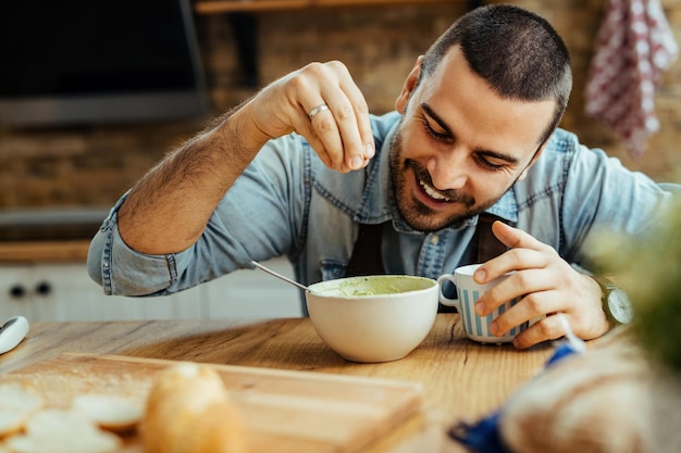 Joven feliz usando sal mientras prepara comida en la cocina.