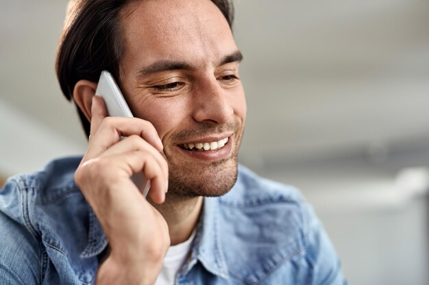 Joven feliz usando un teléfono inteligente mientras hace una llamada telefónica en casa