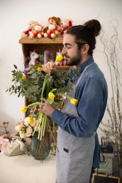 Joven florista masculino que huele los tulipanes amarillos en la floristería