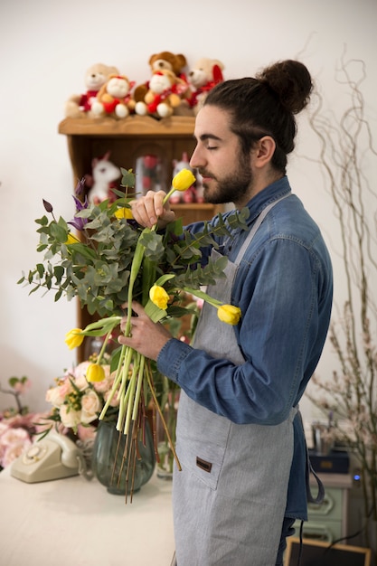 Joven florista masculino que huele los tulipanes amarillos en la floristería