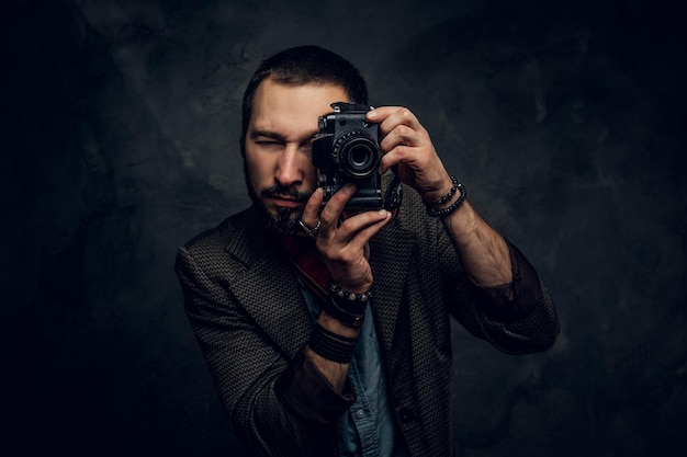 El joven fotógrafo enfocado está tomando una foto en el fondo oscuro del grunge.