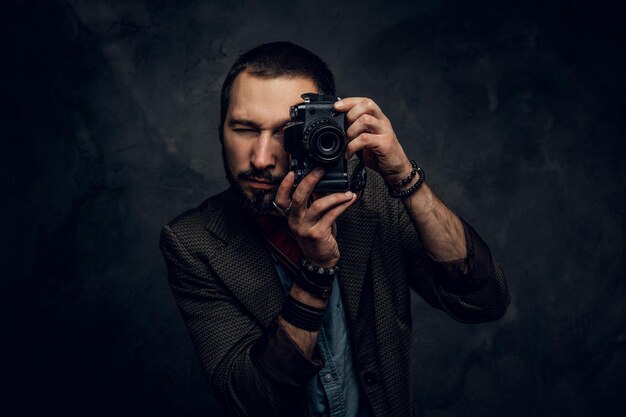 El joven fotógrafo enfocado está tomando una foto en el fondo oscuro del grunge.