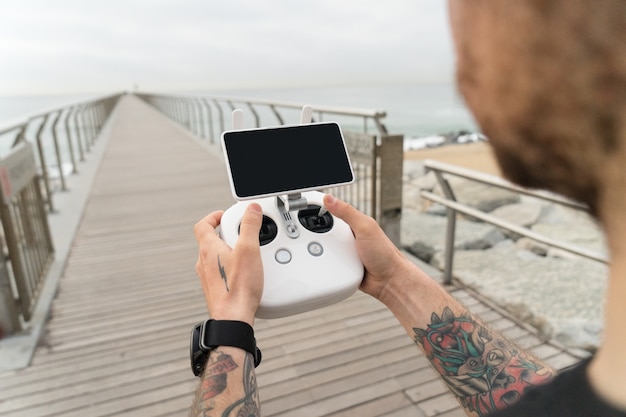 Joven fotógrafo profesional o aficionado o piloto de drones sostiene el panel de control remoto con pantalla y controles listos para volar en quadrocopter en el aire para ver el punto de vista de las aves.