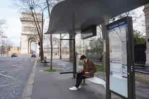 Foto gratuita joven francés esperando en la estación el autobús y usando su teléfono inteligente
