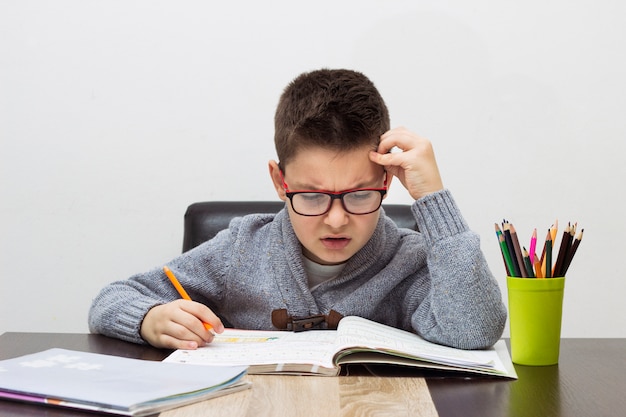 Joven frustrado sobre la tarea, escribiendo en casa. Muchacho que estudia en la tabla. Niño de dibujo con un lápiz.